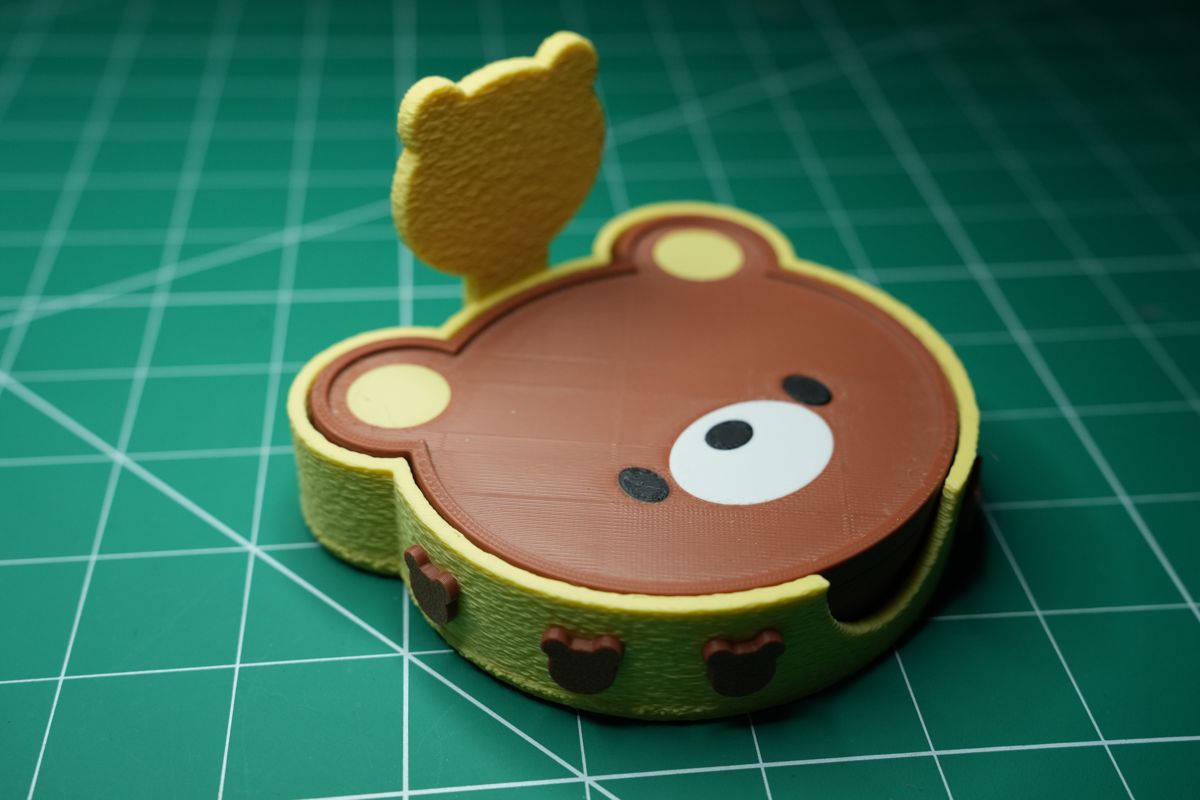 A bear coaster sitting in its yellow holder, the little bear standing on the back