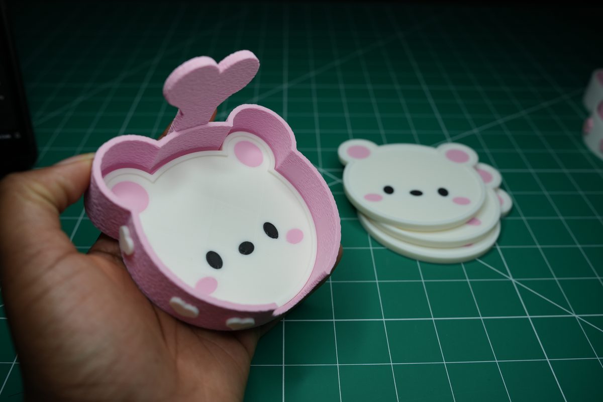 The pink holder in a hand with a coaster inside, white heart charms on its side
